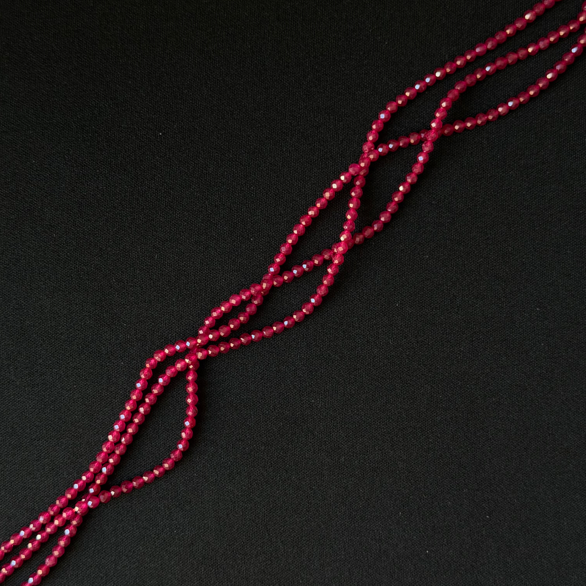 A close-up of a long strand of small faceted red beads arranged diagonally on a dark black background.