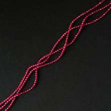 A close-up of a long strand of small faceted red beads arranged diagonally on a dark black background.