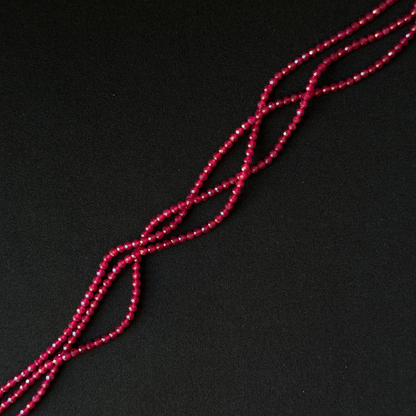 A close-up of a long strand of small faceted red beads arranged diagonally on a dark black background.