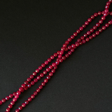 Faceted dark red beads strung on three strands, arranged diagonally on a dark black background.