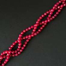 Faceted round beads in a deep berry pink color, arranged in diagonal strands on a dark textured background.
