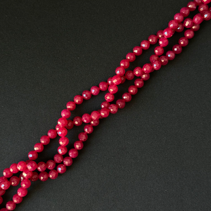 Faceted round beads in a deep berry pink color, arranged in diagonal strands on a dark textured background.