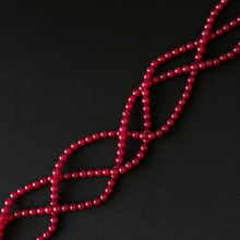 A close-up of a red beaded strand arranged in a crisscross pattern against a solid black background.