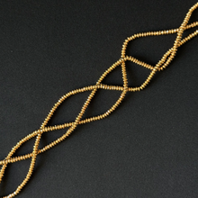 A strand of small gold-colored seed beads arranged in a braided or twisted pattern on a dark, textured background.