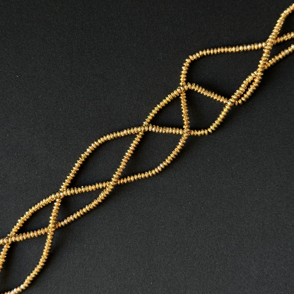 A strand of small gold-colored seed beads arranged in a braided or twisted pattern on a dark, textured background.